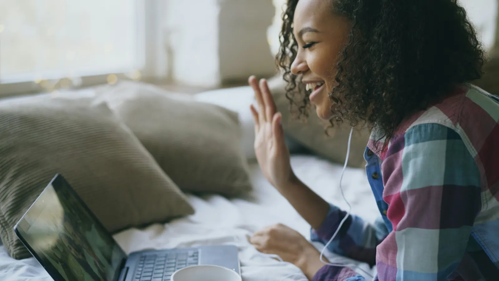 A young woman smiling and waving to a friend on a video call