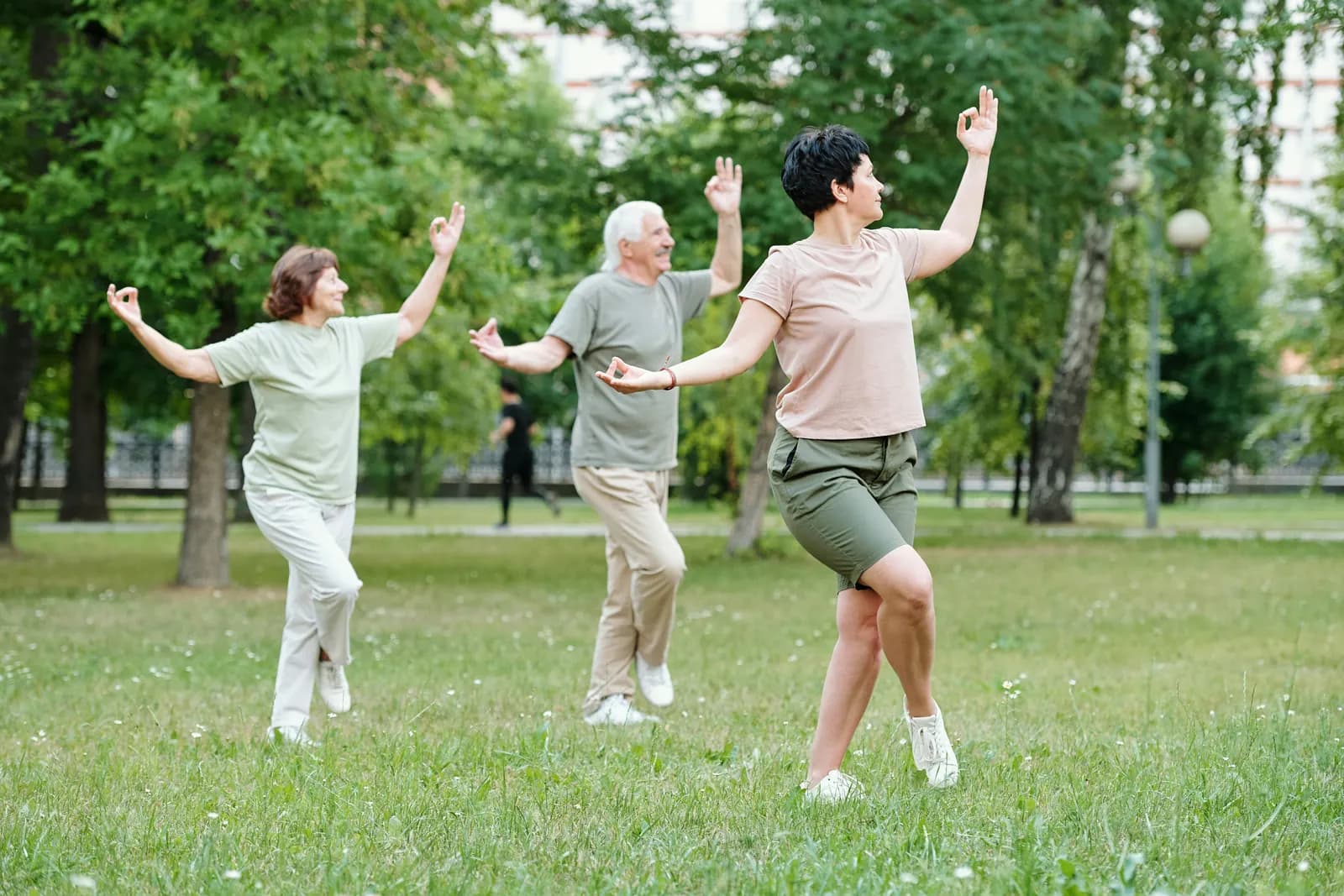 Three older adults doing tai chi together in a park