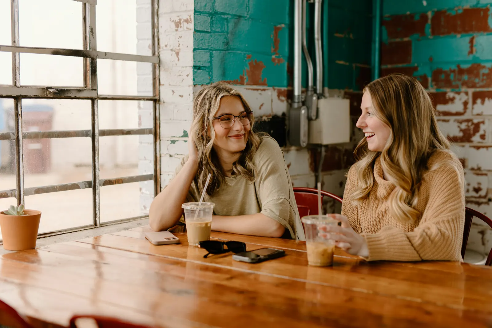 Two friends laughing over iced coffee at a café table