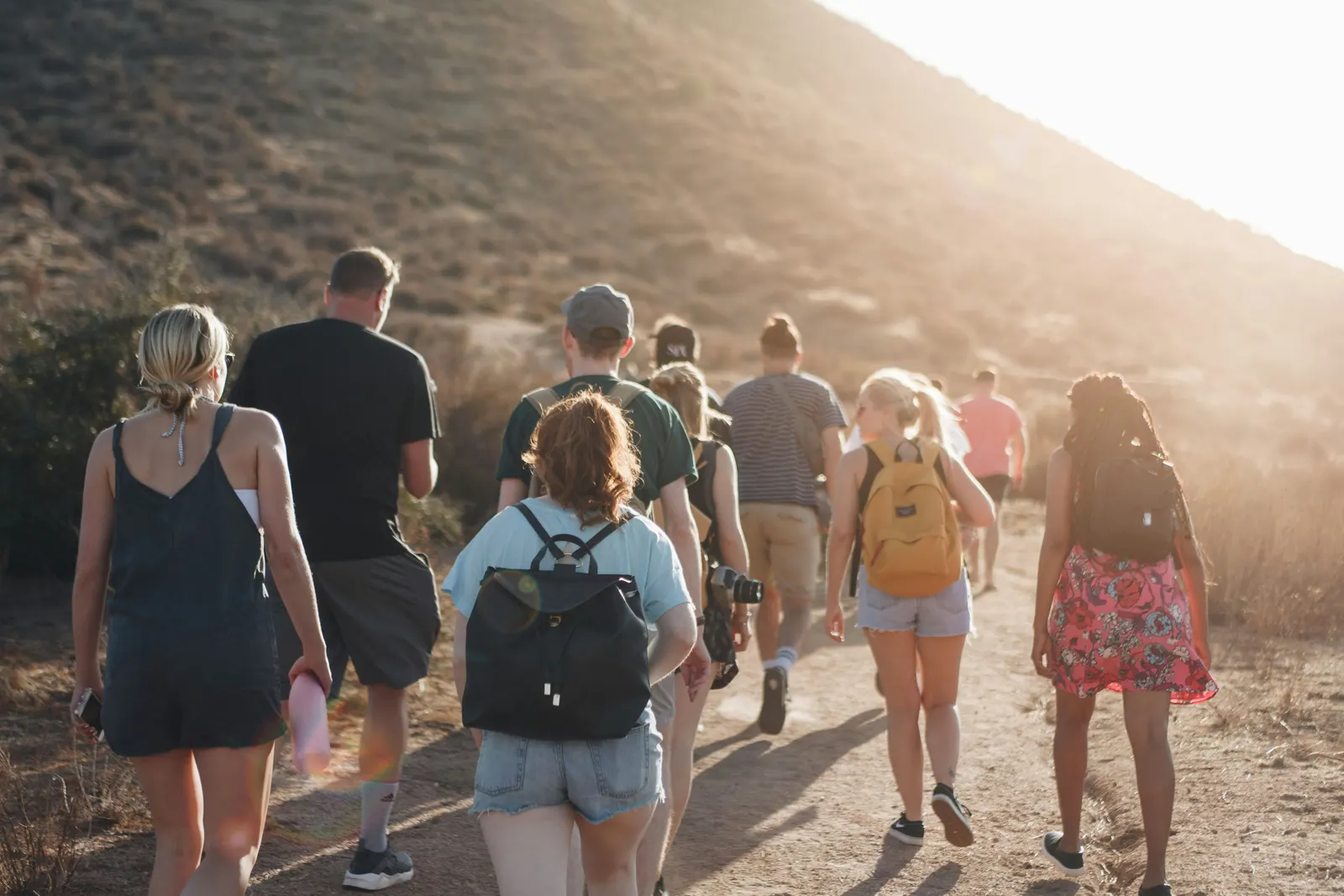 A group of friends walking together on a sunny hillside trail