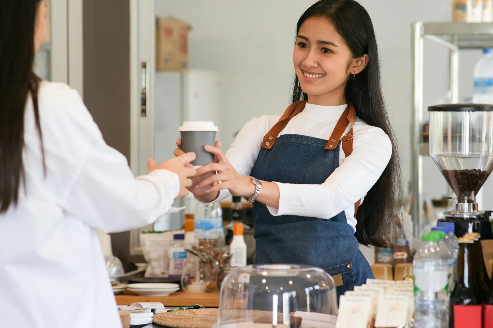 A barista smiling as she hands a coffee to a customer